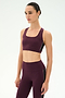 A person wearing the SPLITS59 Lexi Rigor Bra in Dark Cherry/Black, paired with matching leggings made from soft spandex and nylon, stands against a plain white background and gazes slightly to the side.