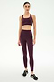 A woman stands in a studio against a plain white background, wearing the SPLITS59 Lexi Rigor Bra in Dark Cherry/Black paired with matching leggings and black sneakers.