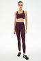 A woman stands in a studio against a plain white background, wearing the SPLITS59 Lexi Rigor Bra in Dark Cherry/Black paired with matching leggings and black sneakers.