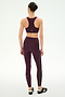 A person stands facing away, wearing the SPLITS59 Lexi Rigor Bra in Dark Cherry/Black paired with matching leggings made from a soft nylon-spandex blend featuring white side stripes, and black athletic shoes, set against a plain white background.