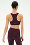A woman with dark hair in a bun is shown from the back against a plain background, wearing the SPLITS59 Lexi Rigor Bra in Dark Cherry/Black, paired with matching leggings.