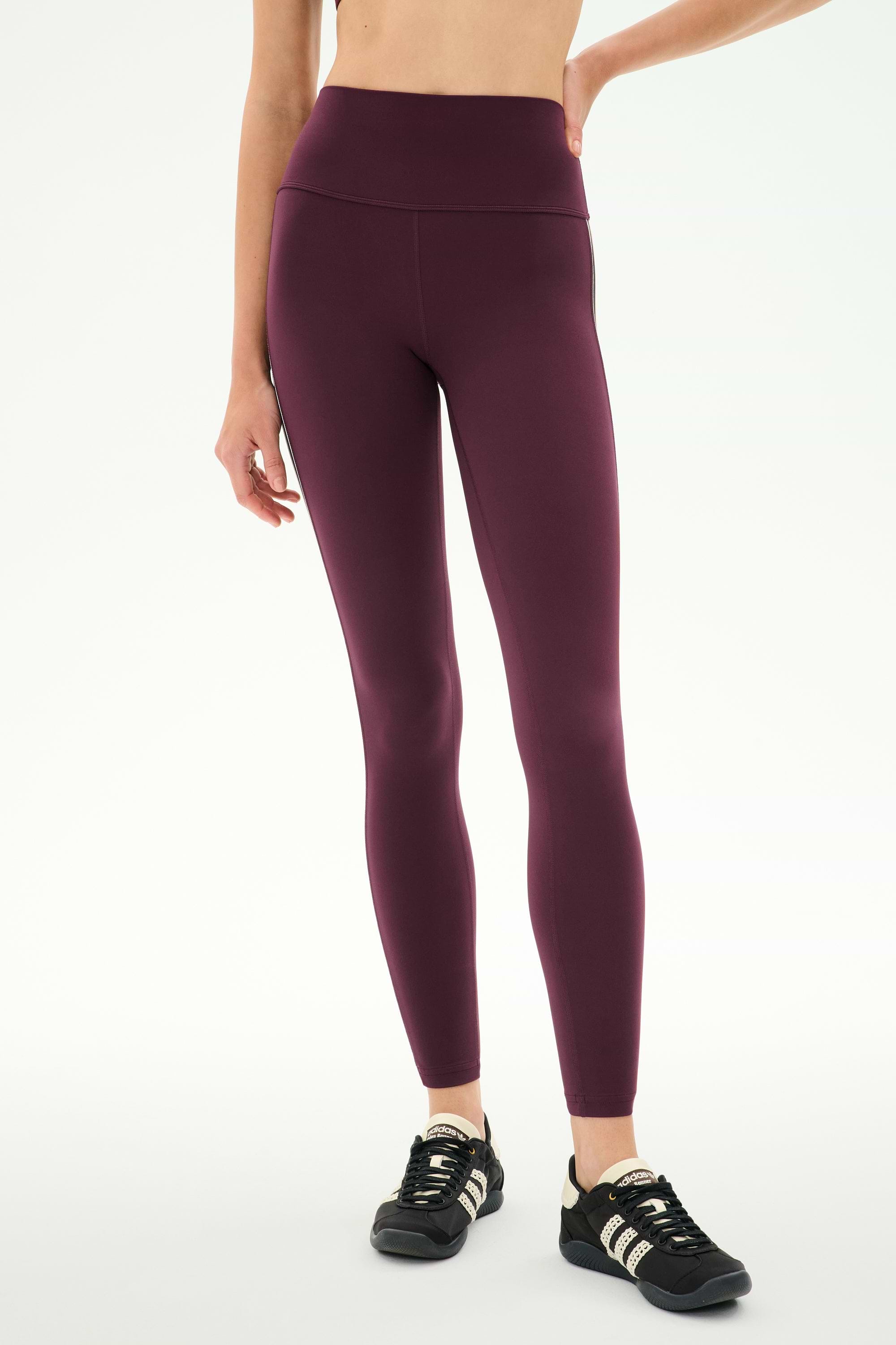 A person wearing SPLITS59 Margot Rigor Legging in Dark Cherry/Black, crafted from high-performance fabric, paired with black athletic shoes and standing against a plain white background—ideal for intense gym workouts.