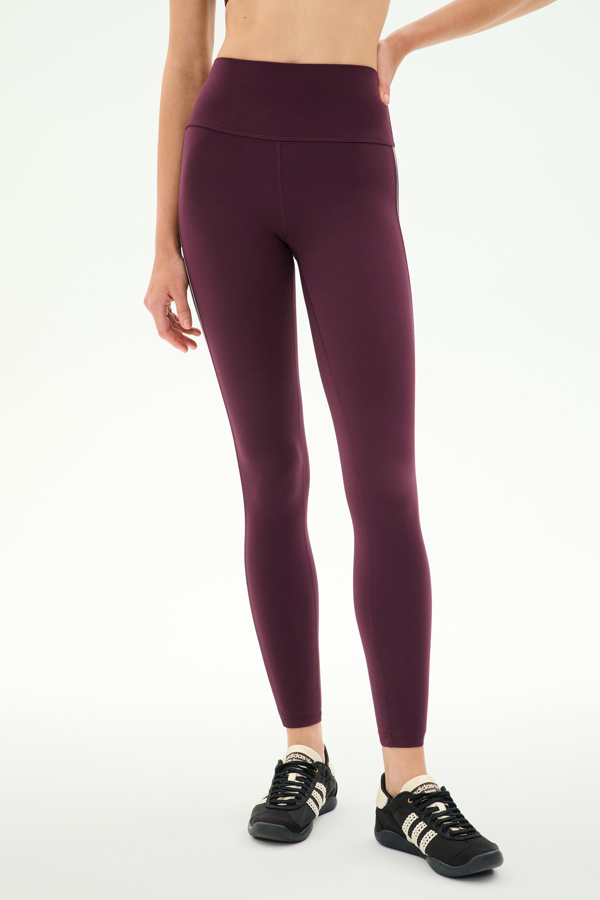A person wearing SPLITS59 Margot Rigor Legging in Dark Cherry/Black, crafted from high-performance fabric, paired with black athletic shoes and standing against a plain white background—ideal for intense gym workouts.