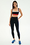 A woman stands against a white background wearing a red, white, and blue striped sports bra, SPLITS59 Monah High Waist Rigor Legging 7/8 in Black/Cobalt, and blue sneakers.