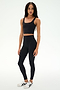 A person stands against a white background, wearing a black crop top, SPLITS59 Sprint High Waist Rigor 7/8 leggings in black, and white sneakers with black stripes.
