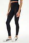 A person is wearing the SPLITS59 Sprint High Waist Rigor 7/8 leggings in black, paired with a black crop top and white sneakers with black stripes, standing against a plain white background.