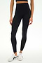 A person wearing SPLITS59's Sprint High Waist Rigor 7/8 leggings in black, paired with a black crop top and white sneakers, stands against a plain white background.
