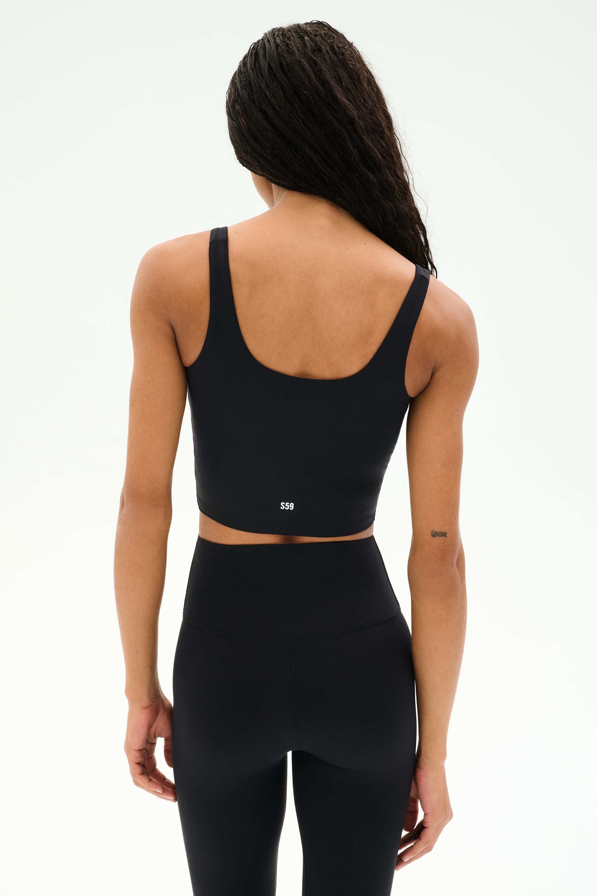 A person stands with their back to the camera, highlighting the SPLITS59 Sprint Rigor Bralette in black paired with high-waisted black leggings, set against a plain light background.