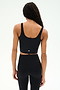 A person stands with their back to the camera, highlighting the SPLITS59 Sprint Rigor Bralette in black paired with high-waisted black leggings, set against a plain light background.