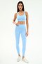 A woman stands against a white background wearing the SPLITS59 Sprint Rigor Bra in Skylight, paired with matching high-waisted leggings and silver sneakers.