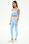 A woman poses against a plain background wearing SPLITS59's Sprint High Waist Rigor 7/8 leggings in Skylight, paired with a matching sports bra and silver sneakers.