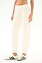 Model wears the SPLITS59 Andie Oversized Fleece Sweatpant - Creme with cream sneakers featuring black stripes, ideal for cool weather workouts, standing against a white backdrop.