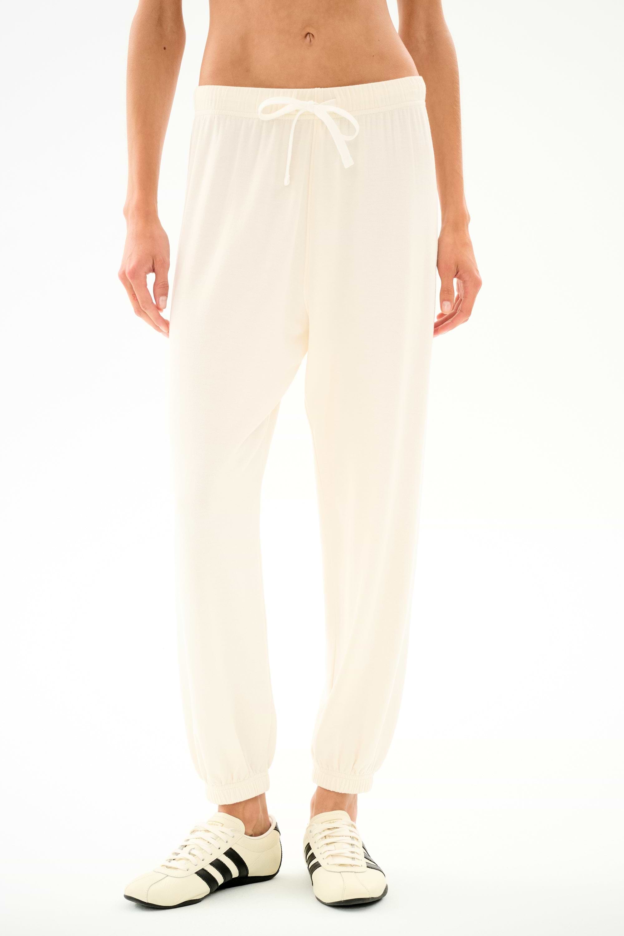 A person models the SPLITS59 Andie Oversized Fleece Sweatpant - Creme, styled with white sneakers against a plain backdrop, ideal for cool weather comfort.