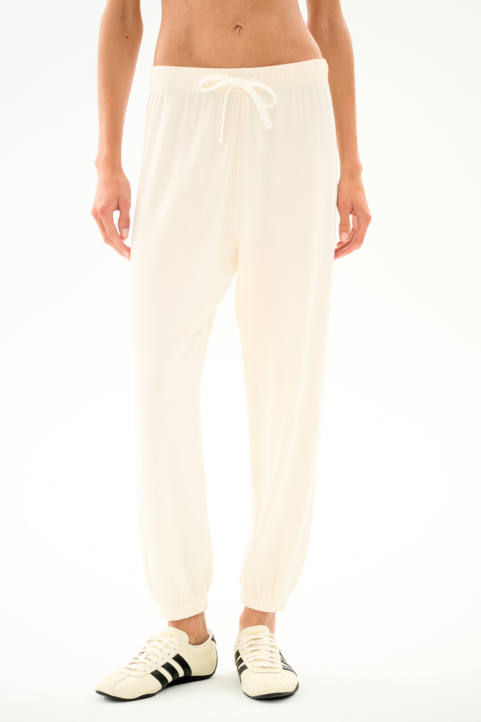 A person models the SPLITS59 Andie Oversized Fleece Sweatpant - Creme, styled with white sneakers against a plain backdrop, ideal for cool weather comfort.