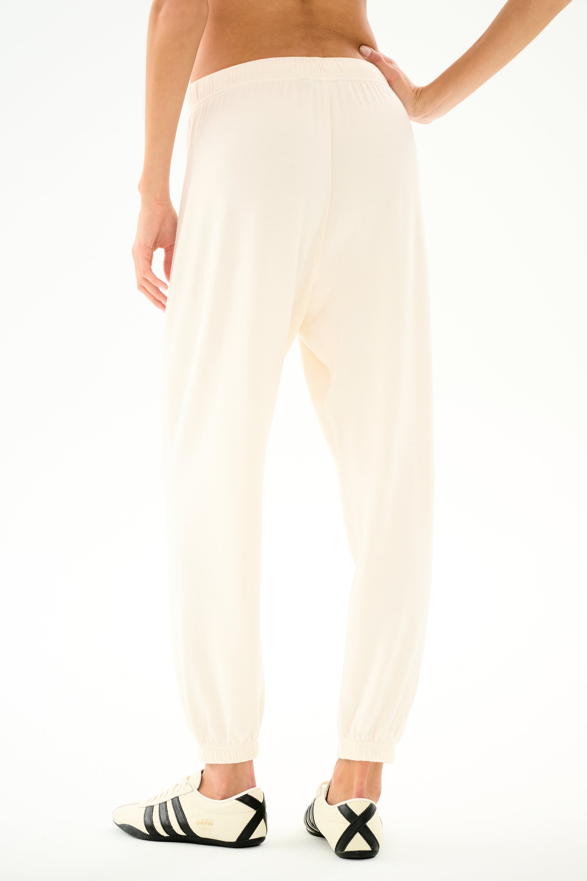 Person wearing SPLITS59 Andie Oversized Fleece Sweatpant - Creme and black-and-white sneakers, ideal for cool weather workouts, standing with back to camera on white background.