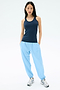 A woman stands against a plain background wearing the SPLITS59 Ashby Rib Tank in Indigo, paired with light blue joggers and white sneakers—an ideal look for gym sessions or laid-back days.
