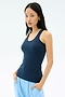 A woman stands with her hands in the pockets of light blue pants, wearing the SPLITS59 Ashby Rib Tank in Indigo, crafted from soft baby rib fabric, against a plain light background.