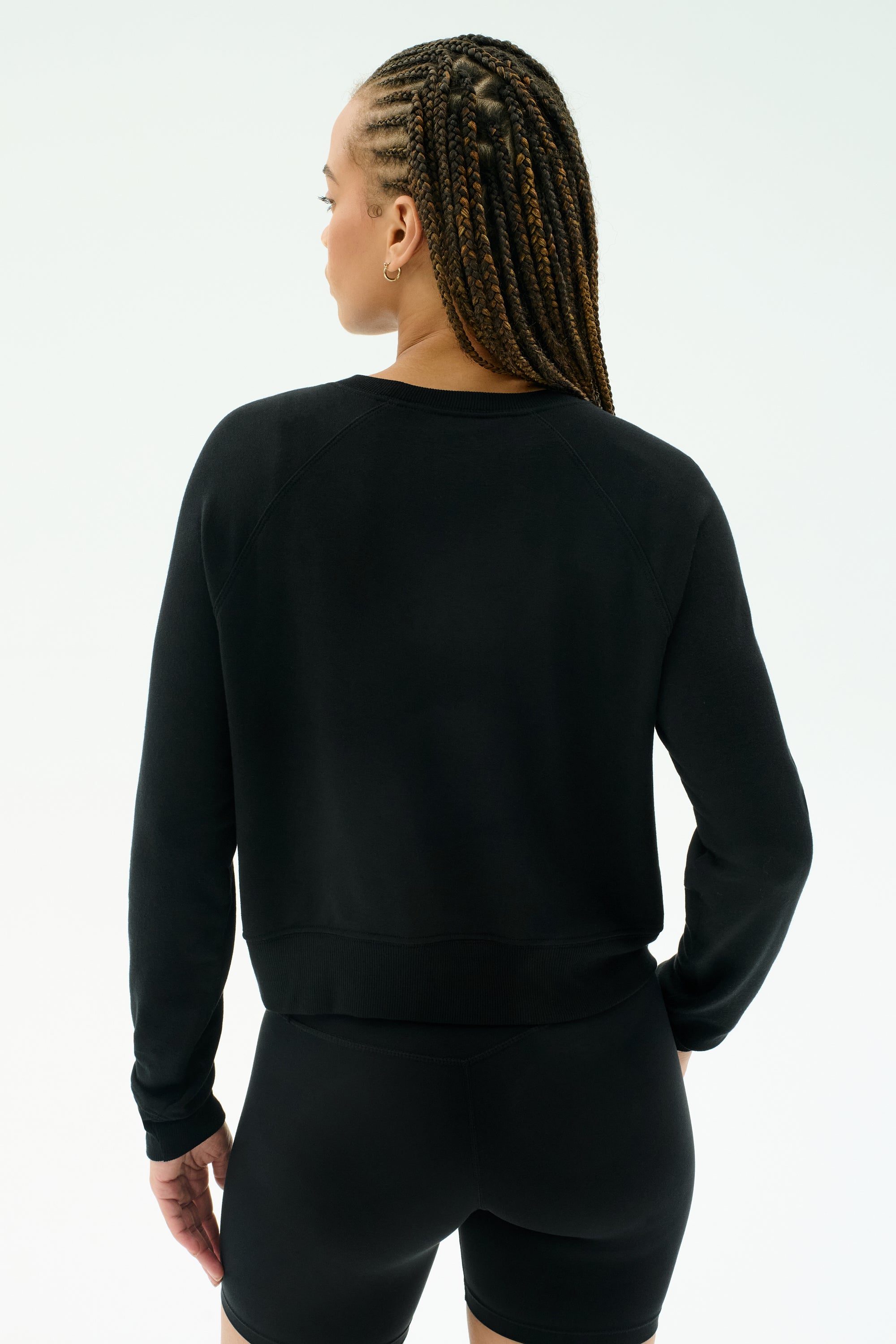 Person with braided hair wears the SPLITS59 Brooks Fleece Long Sleeve Sweatshirt in black, facing away from the camera against a plain light background. Made in Los Angeles for everyday comfort and effortless style.