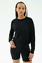 A woman wears the SPLITS59 Brooks Fleece Long Sleeve Sweatshirt in black, paired with fitted shorts, standing against a plain white background. Made in Los Angeles.
