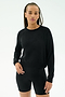 A woman wears the SPLITS59 Brooks Fleece Long Sleeve Sweatshirt in black, paired with fitted shorts, standing against a plain white background. Made in Los Angeles.