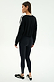 A woman faces slightly away from the camera on a white background, wearing the SPLITS59 Ellie Fleece V Neck Sweatshirt in black/white, paired with black leggings and black athletic shoes.