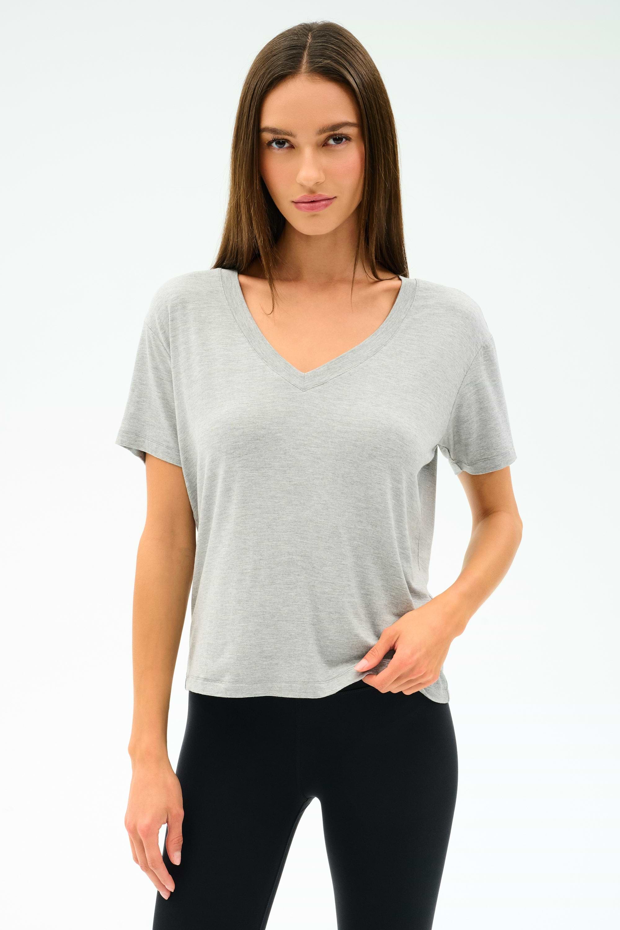 A person faces forward, wearing the SPLITS59 Georgia Jersey V-Neck in Heather Grey and black pants, standing against a plain white background.