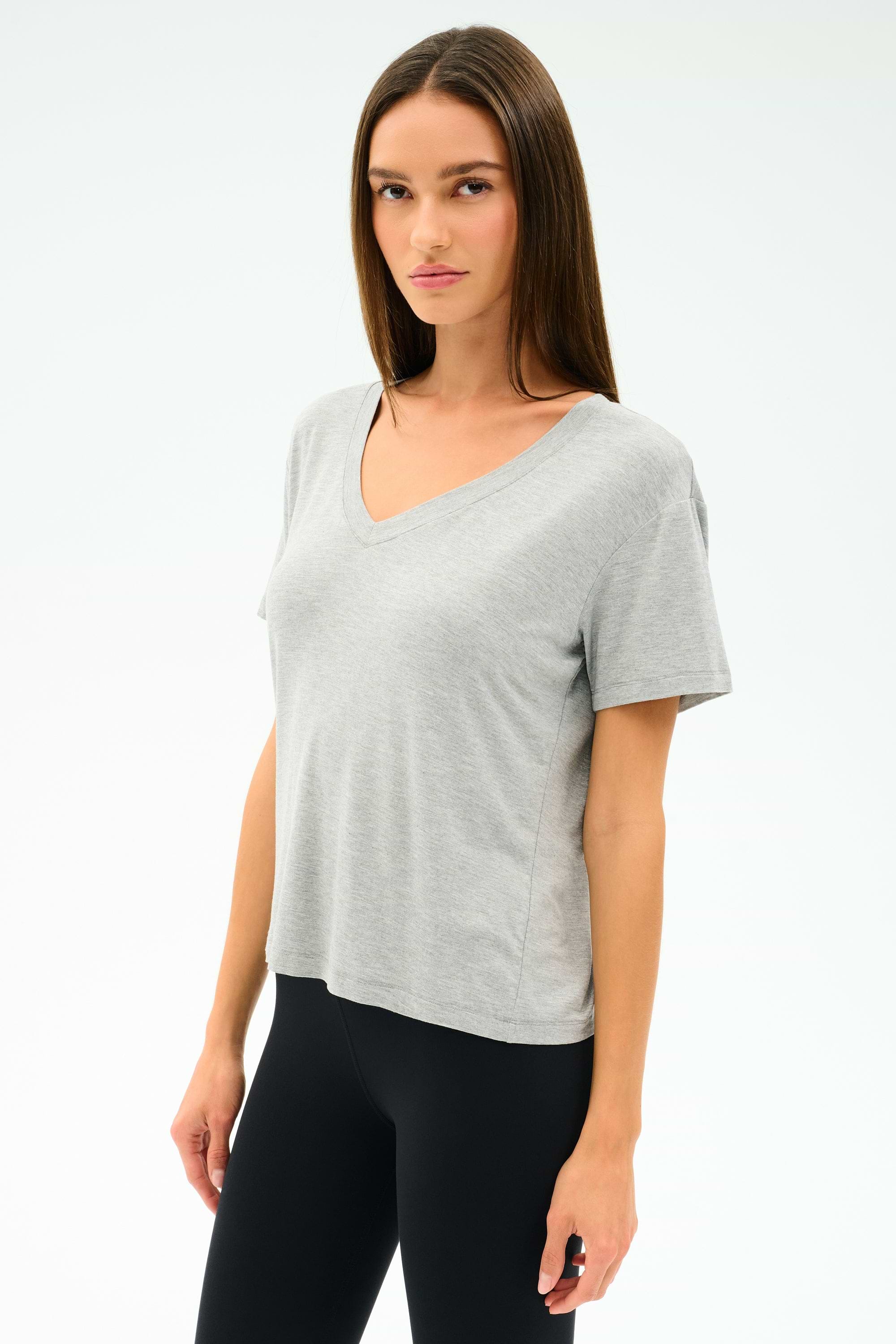 A woman faces forward against a plain white background, wearing the SPLITS59 Georgia Jersey V-Neck in Heather Grey and black spandex leggings.
