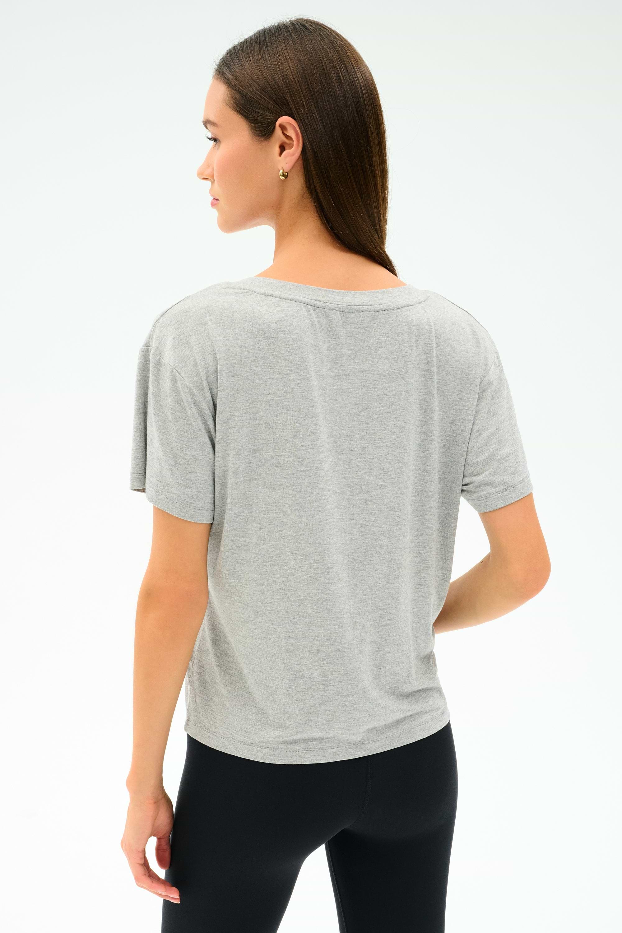 A woman with straight brown hair, wearing the SPLITS59 Georgia Jersey V-Neck in Heather Grey, stands facing away from the camera against a plain light background.