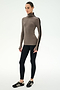 A woman stands against a white background wearing the SPLITS59 Jackson Rib Full Length Turtleneck in Lentil/Black—a soft modal spandex blend top with black striped sleeves—paired with black leggings and black sneakers.