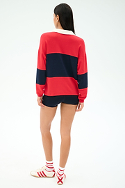 A person stands with their back to the camera, wearing the SPLITS59 Katie Fleece Rugby in Pirate Red/Indigo, black shorts, white socks, and white sneakers with red stripes.