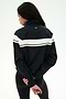 A person stands with their back to the camera, wearing the SPLITS59 Morrison Nylon Twill Track Jacket in Black/Creme, featuring a white stripe across the back, paired with black spandex leggings. Their hands are clasped behind their back.