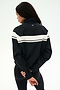 A person stands with their back to the camera, wearing the SPLITS59 Morrison Nylon Twill Track Jacket in Black/Creme, featuring a white stripe across the back, paired with black spandex leggings. Their hands are clasped behind their back.