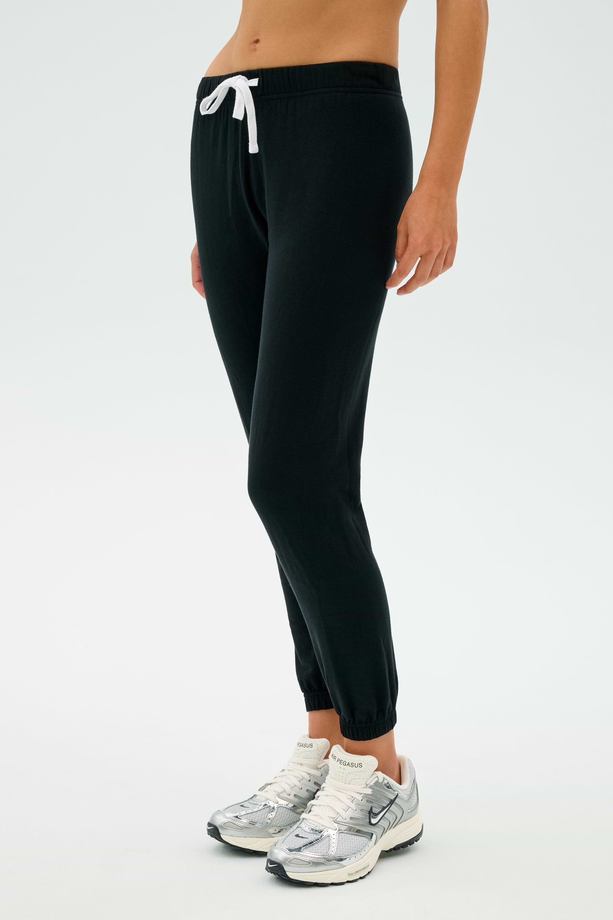 A person in the Sonja Fleece Sweatpant in black from SPLITS59 and white sneakers stands against a light background.