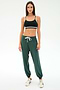 A woman faces forward in a black sports bra, SPLITS59's Andie Oversized Fleece Sweatpant in Military, and white sneakers—ideal for cool weather workouts—set against a plain white background.