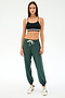 A woman faces forward in a black sports bra, SPLITS59's Andie Oversized Fleece Sweatpant in Military, and white sneakers—ideal for cool weather workouts—set against a plain white background.