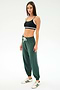 A woman stands against a plain background in a black sports bra, SPLITS59 Andie Oversized Fleece Sweatpant in Military, and white sneakers with green stripes—ideal for warm weather workouts.