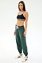 A woman stands against a plain background in a black sports bra, SPLITS59 Andie Oversized Fleece Sweatpant in Military, and white sneakers with green stripes—ideal for warm weather workouts.