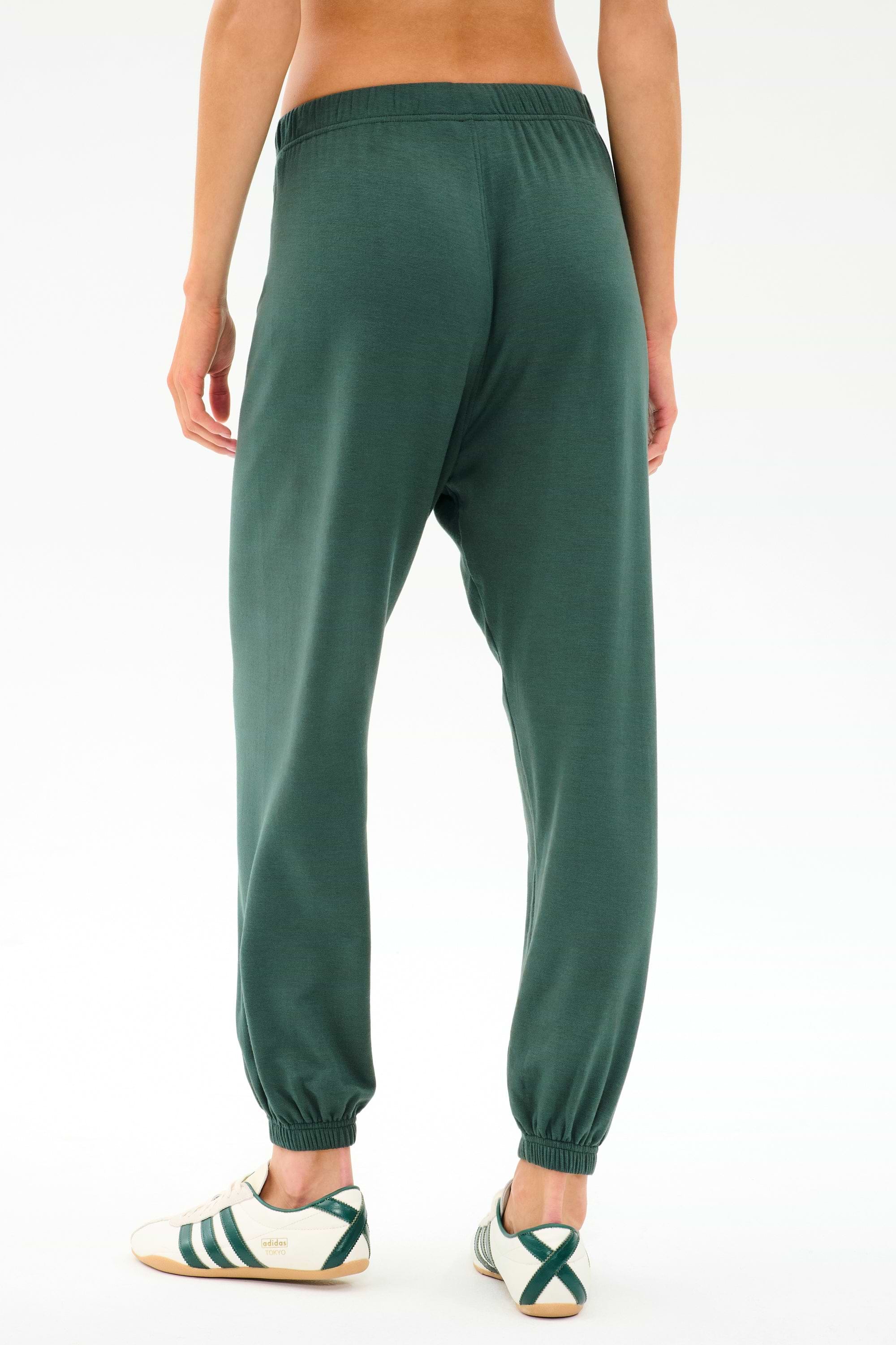 Person wearing SPLITS59 Andie Oversized Fleece Sweatpant in Military and white sneakers with green stripes, shown from the back on a plain white background—ideal for cool weather workouts or laid-back days.