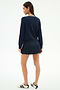 A woman stands facing away against a white background, wearing the SPLITS59 Shira Woven Pleated Skort in Indigo and a navy sweater, paired with white sneakers featuring dark stripes.