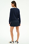 A woman stands facing away against a white background, wearing the SPLITS59 Shira Woven Pleated Skort in Indigo and a navy sweater, paired with white sneakers featuring dark stripes.