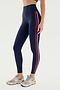 A person wears SPLITS59's Ella High Waist Airweight 7/8 leggings in Indigo/P Red with beige sneakers, standing against a white background, poised for hot yoga.
