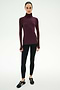 A woman wears the SPLITS59 Jackson Rib Full Length Turtleneck in Dark Cherry/Creme—a maroon top with white striped sleeves, crafted from soft modal fabric—paired with black leggings and black sneakers, standing against a plain white background.