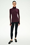 A woman wears the SPLITS59 Jackson Rib Full Length Turtleneck in Dark Cherry/Creme—a maroon top with white striped sleeves, crafted from soft modal fabric—paired with black leggings and black sneakers, standing against a plain white background.