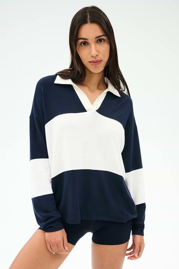 A woman wears the SPLITS59 Katie Fleece Rugby in Indigo/White with navy shorts, standing against a plain light background.