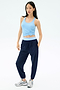 A woman faces forward against a white background, wearing the SPLITS59 Megan Woven Nylon Jogger in Indigo, a light blue knotted tank top, and gray sneakers.