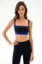 Woman with long brown hair wears the Monah Rigor Bra - Black/Cobalt by SPLITS59, standing with one hand on her hip against a plain light background.