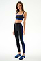 Woman wears the SPLITS59 Clare High Waist Rigor 7/8 - Black/Cobalt leggings with matching sports bra and blue sneakers, posed against a white background.