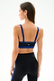 A woman stands with her back to the camera, wearing the SPLITS59 Monah Rigor Bra - Black/Cobalt and black leggings with blue side stripes.