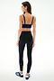 Woman stands with back to camera wearing SPLITS59 Clare High Waist Rigor 7/8 - Black/Cobalt leggings, blue-striped sports bra, and blue athletic shoes on a plain background.