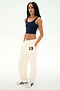 A woman stands against a white background wearing a navy crop top, white sneakers with black stripes, and SPLITS59 Serena French Terry Oversized Sweatpant in Creme/59—crafted from soft cotton and featuring "59" on the hip.